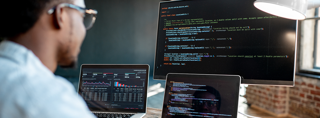 Programmer works with code across three monitors.